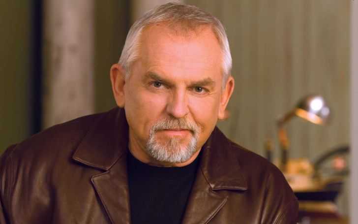 John Ratzenberger in a brown coat and black t-shirt.