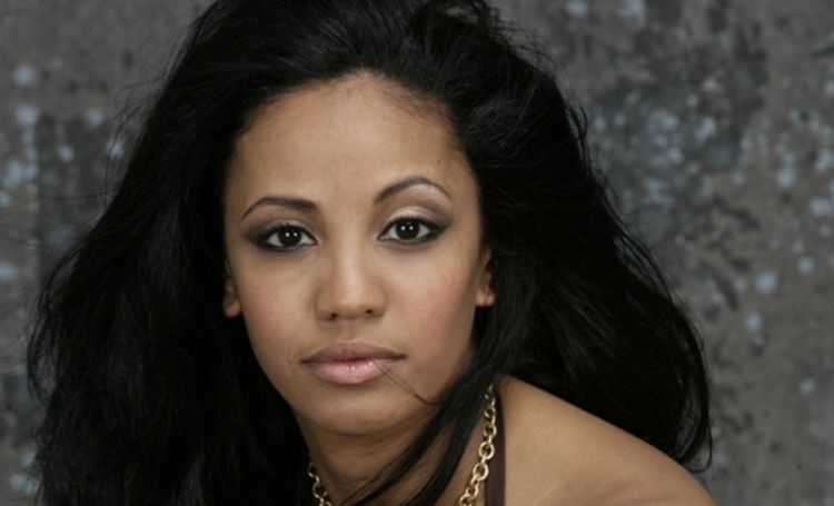 Jodie Resther, black hair and wearing necklace looks at camera.