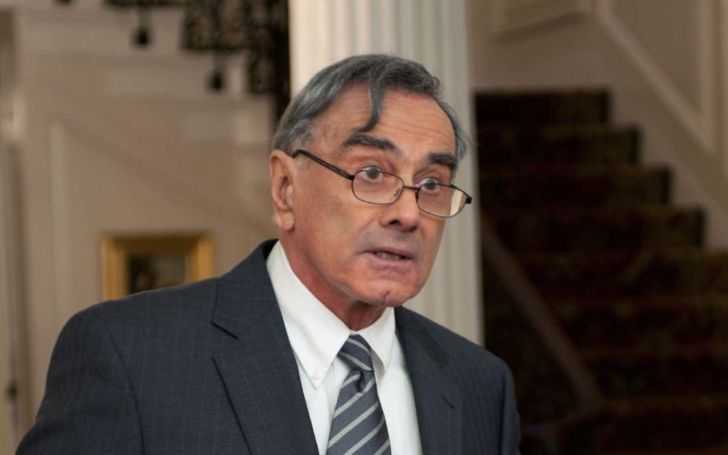 Dan Hedaya in a black suit and black tie.