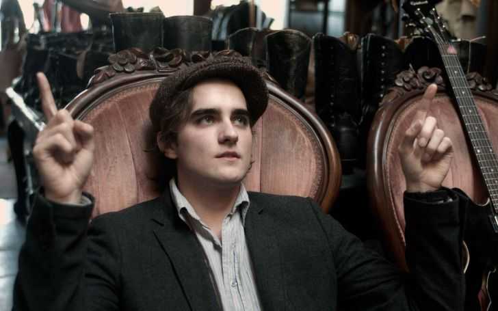 Landon Liboiron wearing a cap and a black suit.