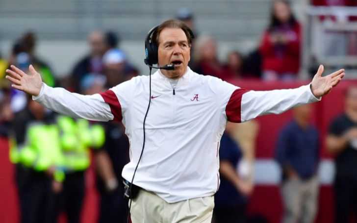Nick Saban in a white jacket and headsets on ears.
