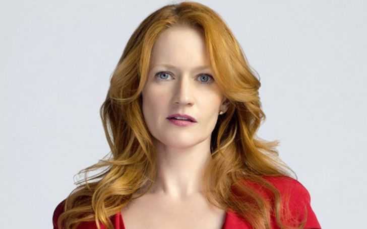 Paula Malcomson with auburn hair and blue eyes wearing a red dress.